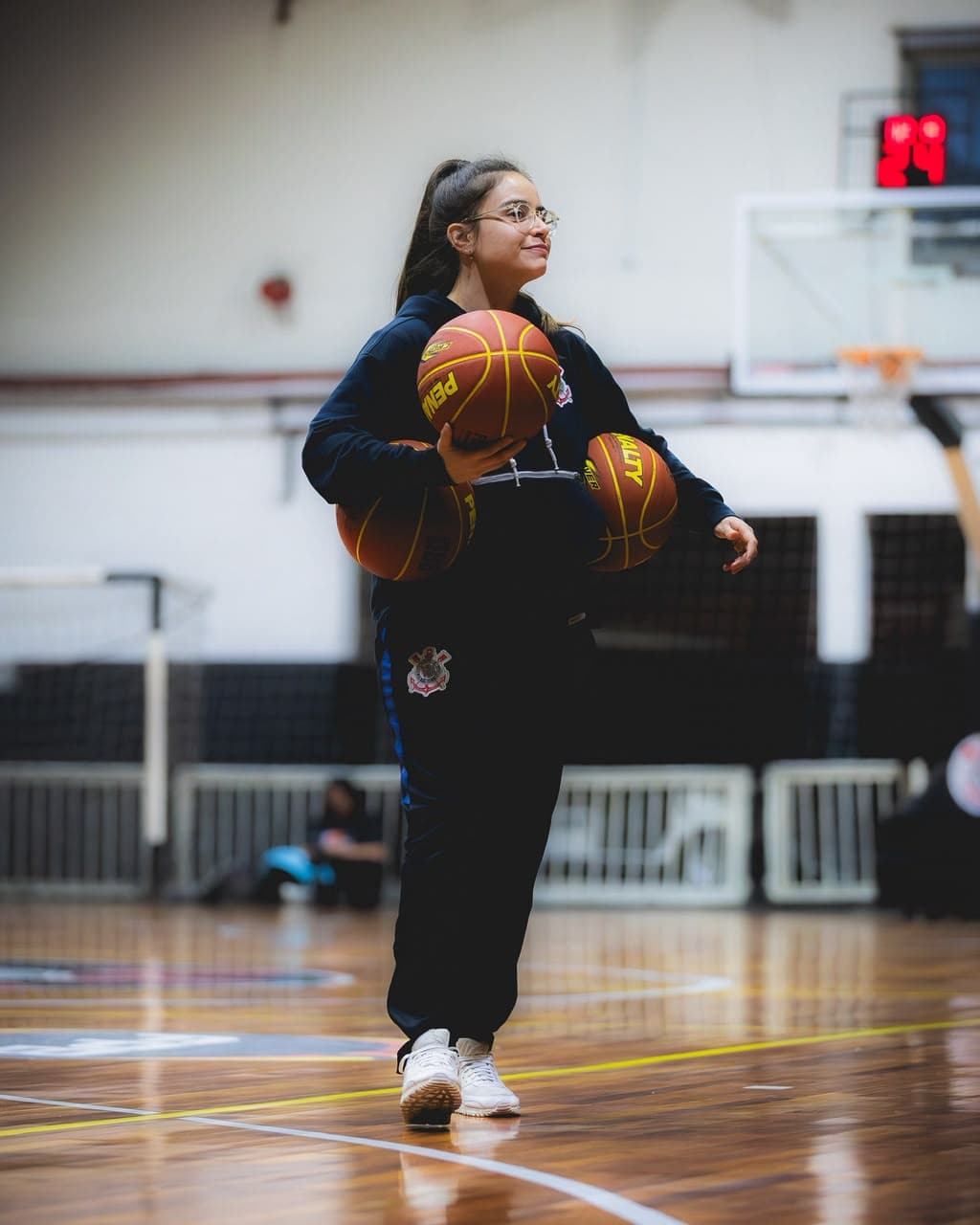 Joana Paiva walking across the court carrying three basketballs before training.